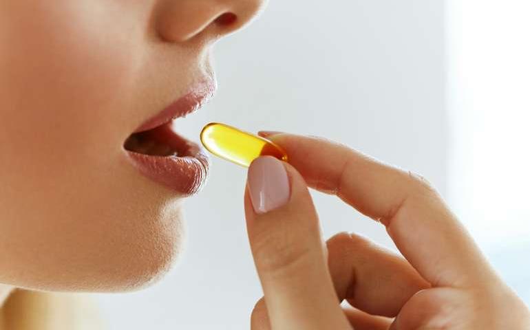 Female consumer taking omega-3 softgel dietary supplement